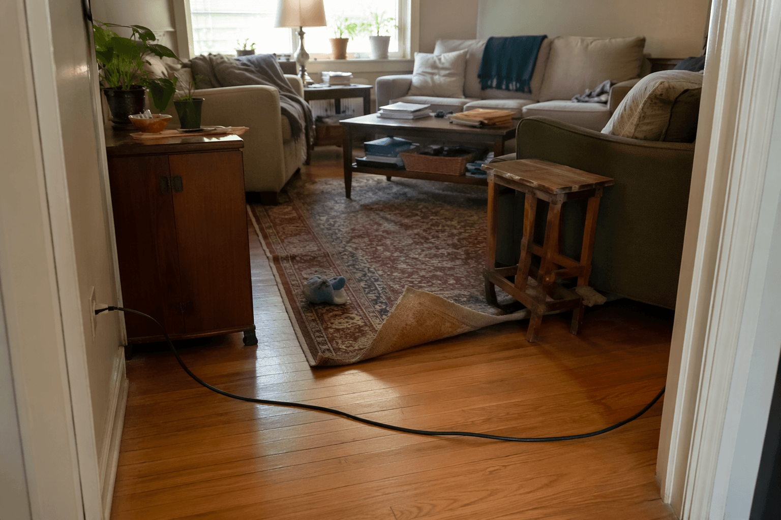 Living room with a curled rug edge, an electrical cord across the walkway, and clutter near a coffee table