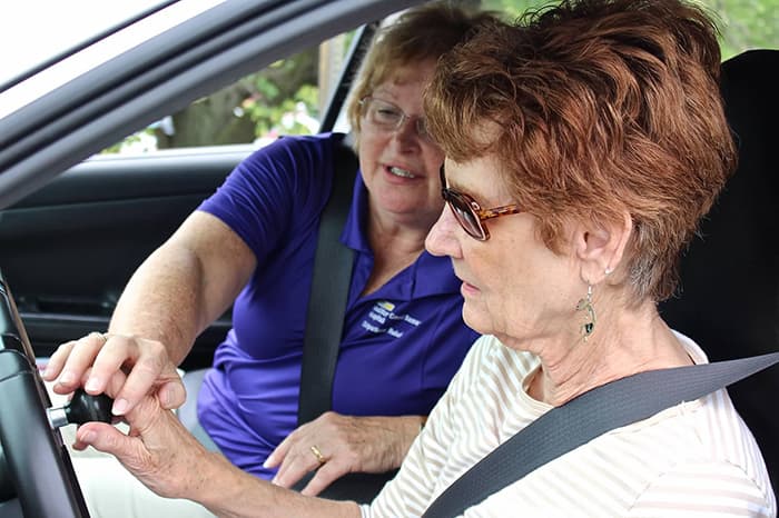 An older female driver working with an occupational therapist during an in-car driving rehabilitation evaluation, focused on an adaptive steering wheel.