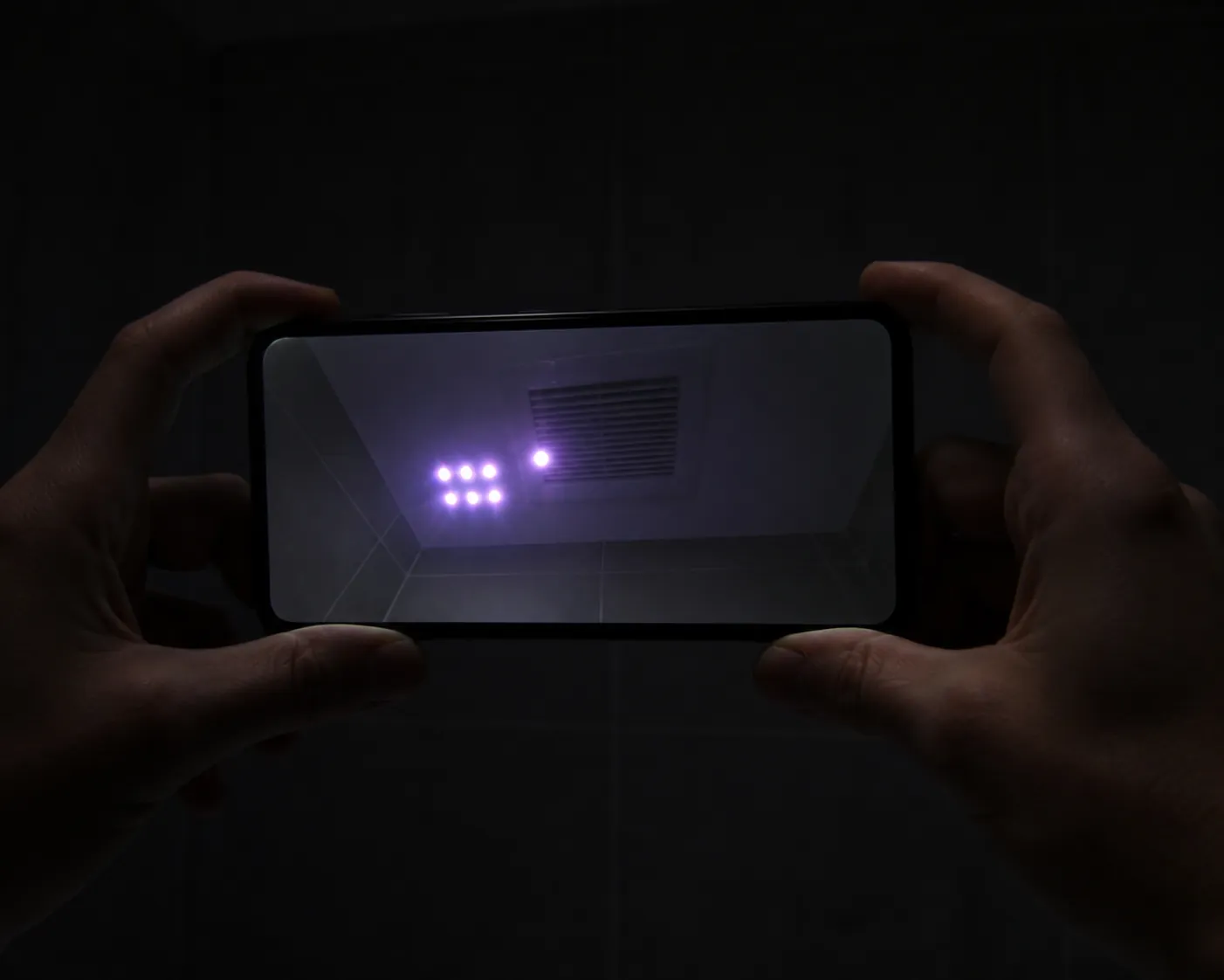 Smartphone screen showing bright white and purple dots near a bathroom vent during infrared detection