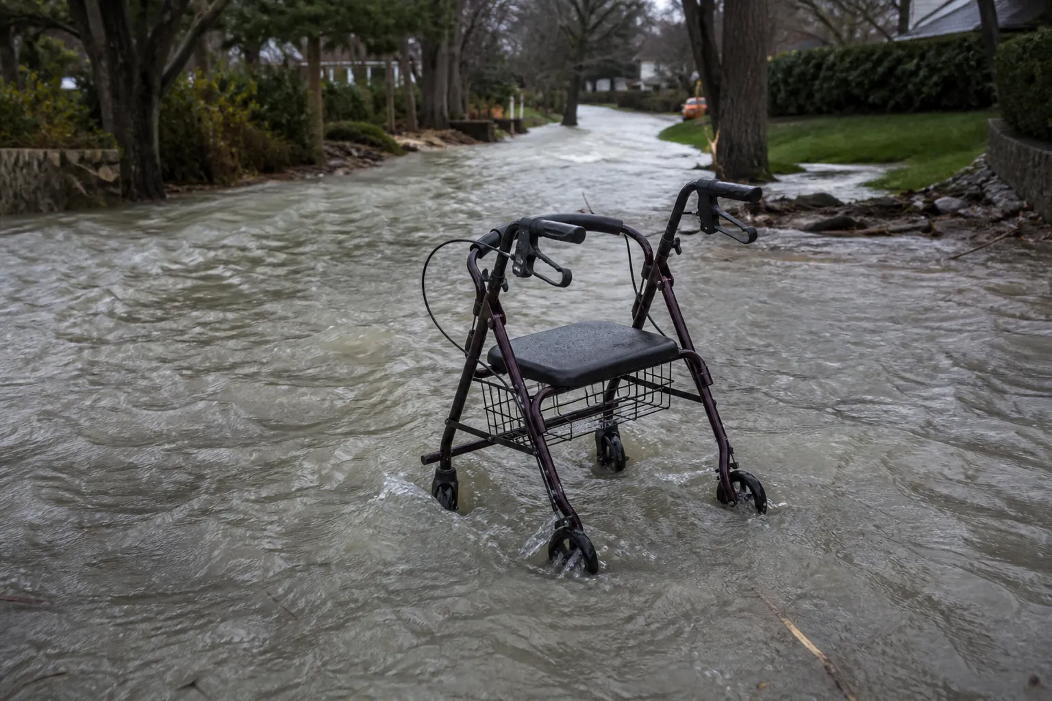 Fast-moving ankle-deep floodwater swirling around a rollator walker on a suburban walkway
