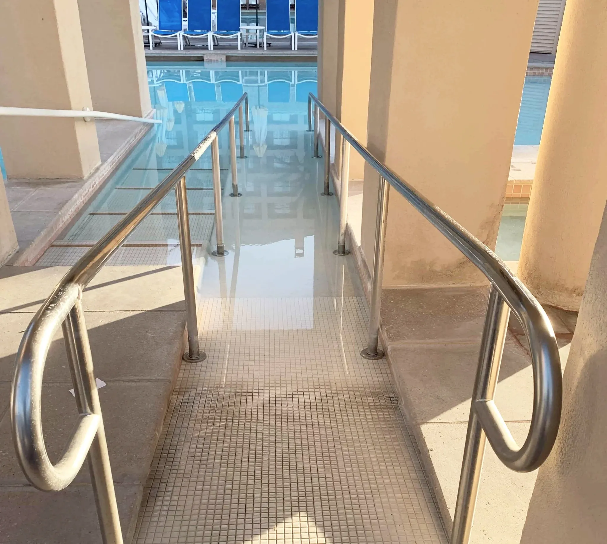Accessible sloped pool entry with a gradual ramp descending into the water and handrails along the side