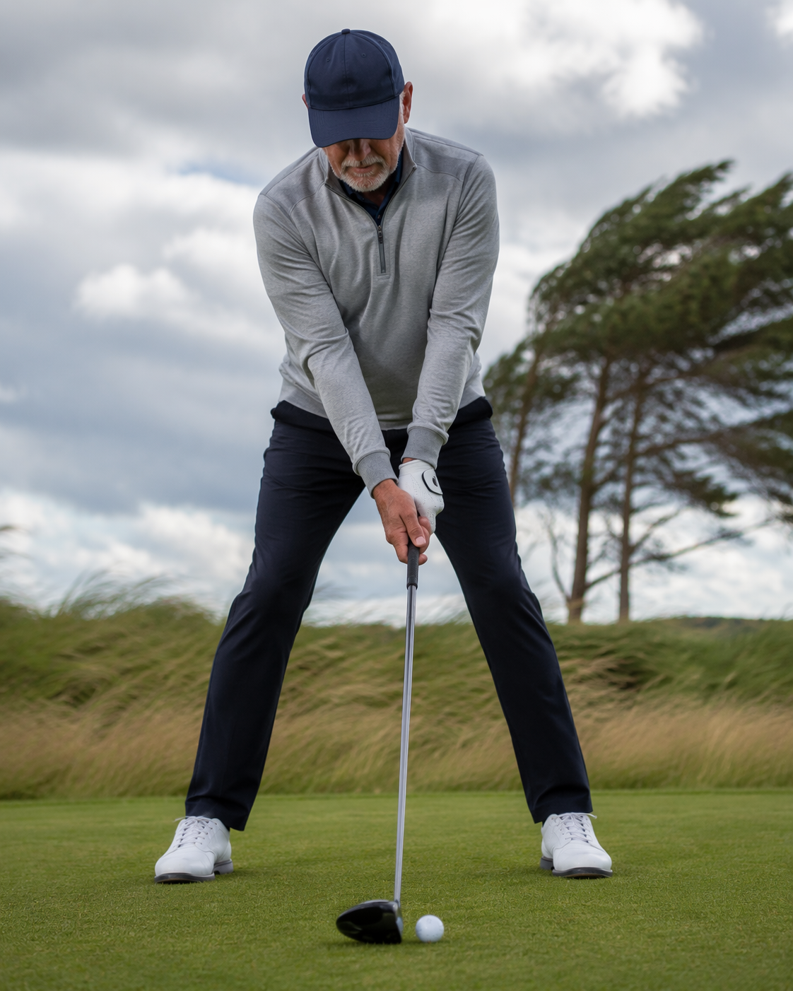 Close-up of a senior golfer using a wide stance, lower tee, ball slightly back, and hands gripping down