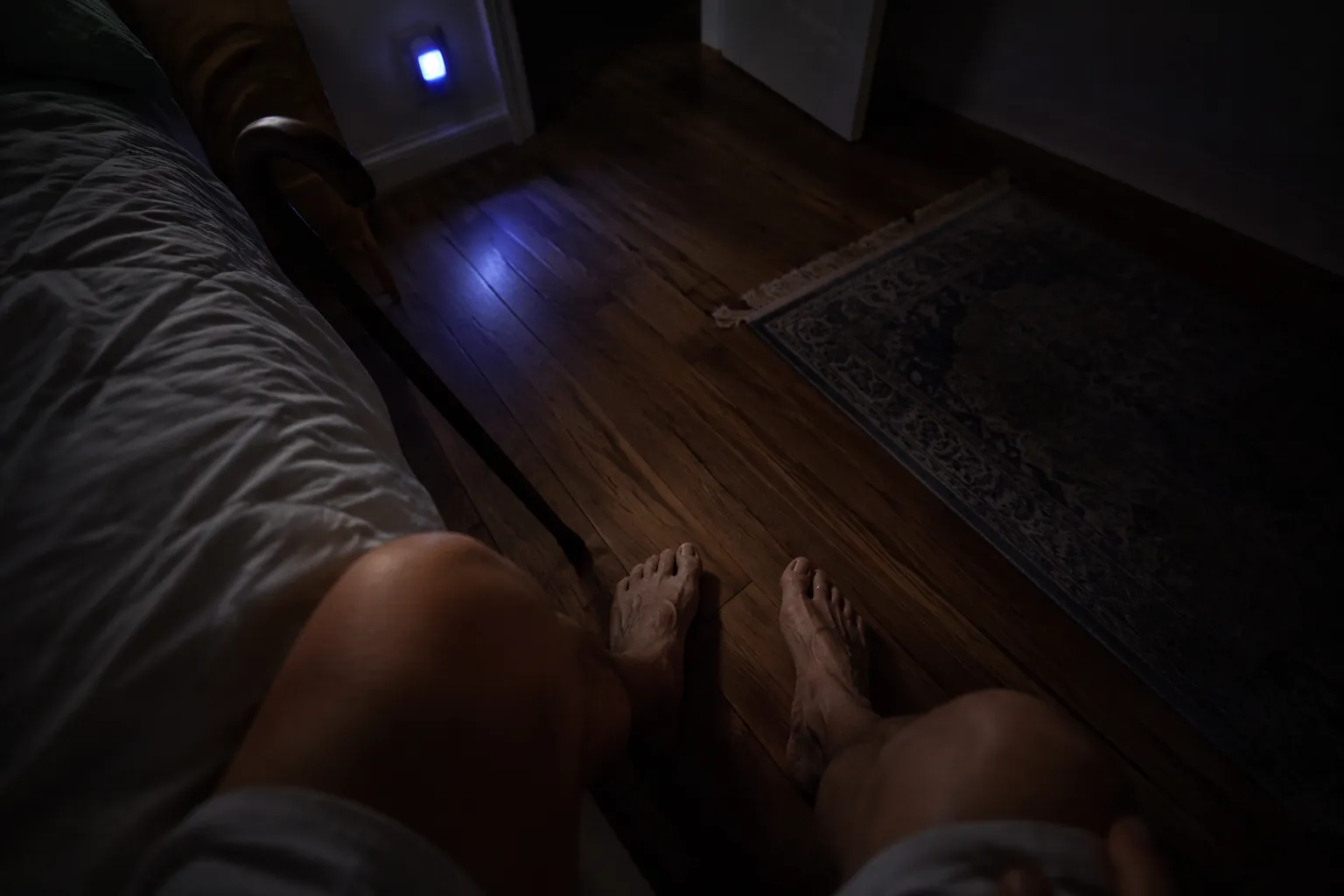Older adult feet on a bedroom floor near an askew rug and cane in low nightlight
