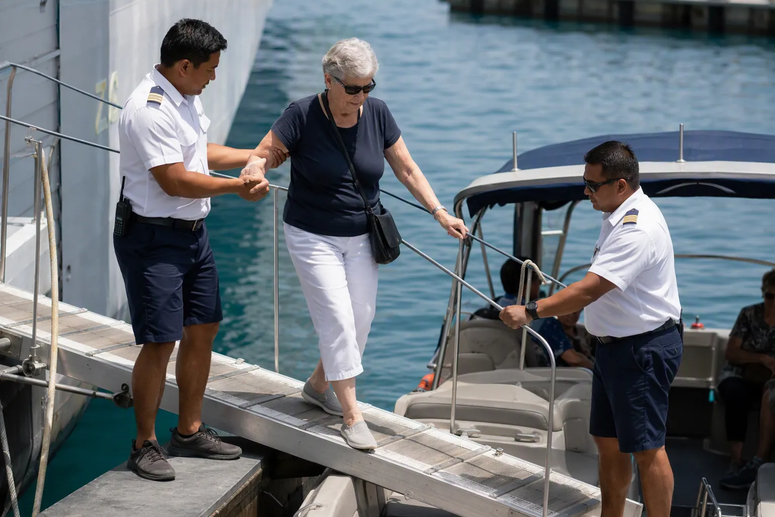 Cruise crew member helping an older traveler down an inclined gangway toward a tender boat