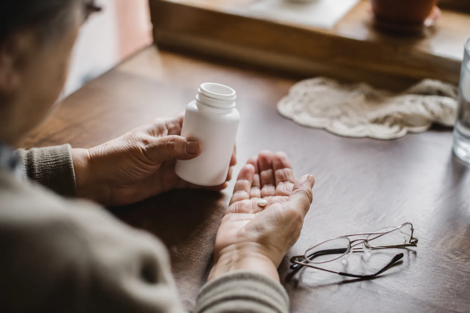 Older adult hands checking a medication bottle and pill on a kitchen table