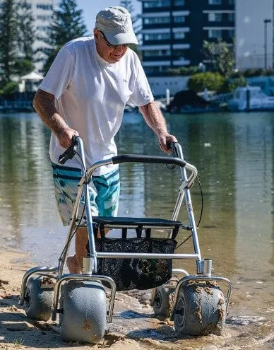 All-terrain beach rollator with large wheels being pushed across sand near the ocean