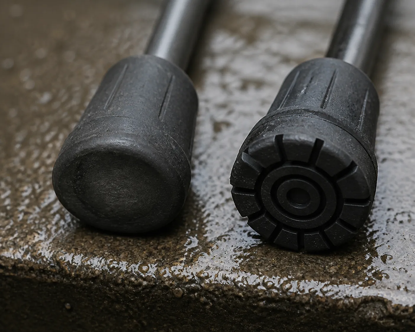 Two walking-cane rubber tips on a wet concrete step, one worn smooth and one with fresh tread
