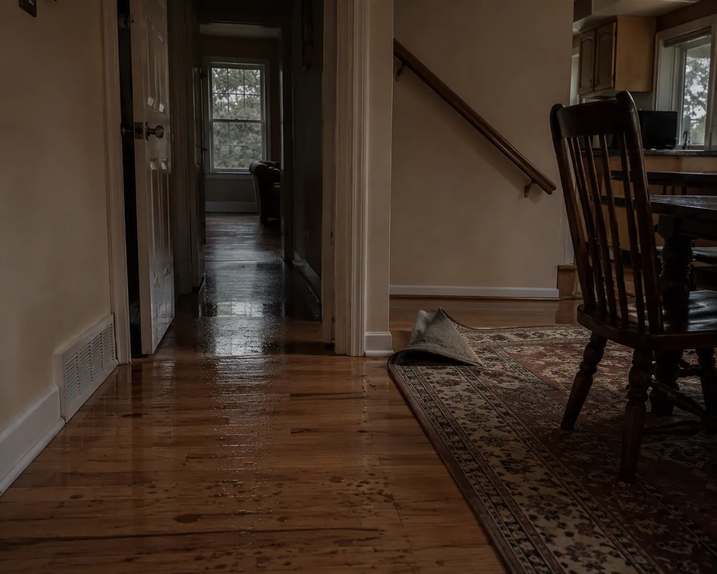 Dim hallway with wet spots, a curled rug, and a chair out of place after a storm