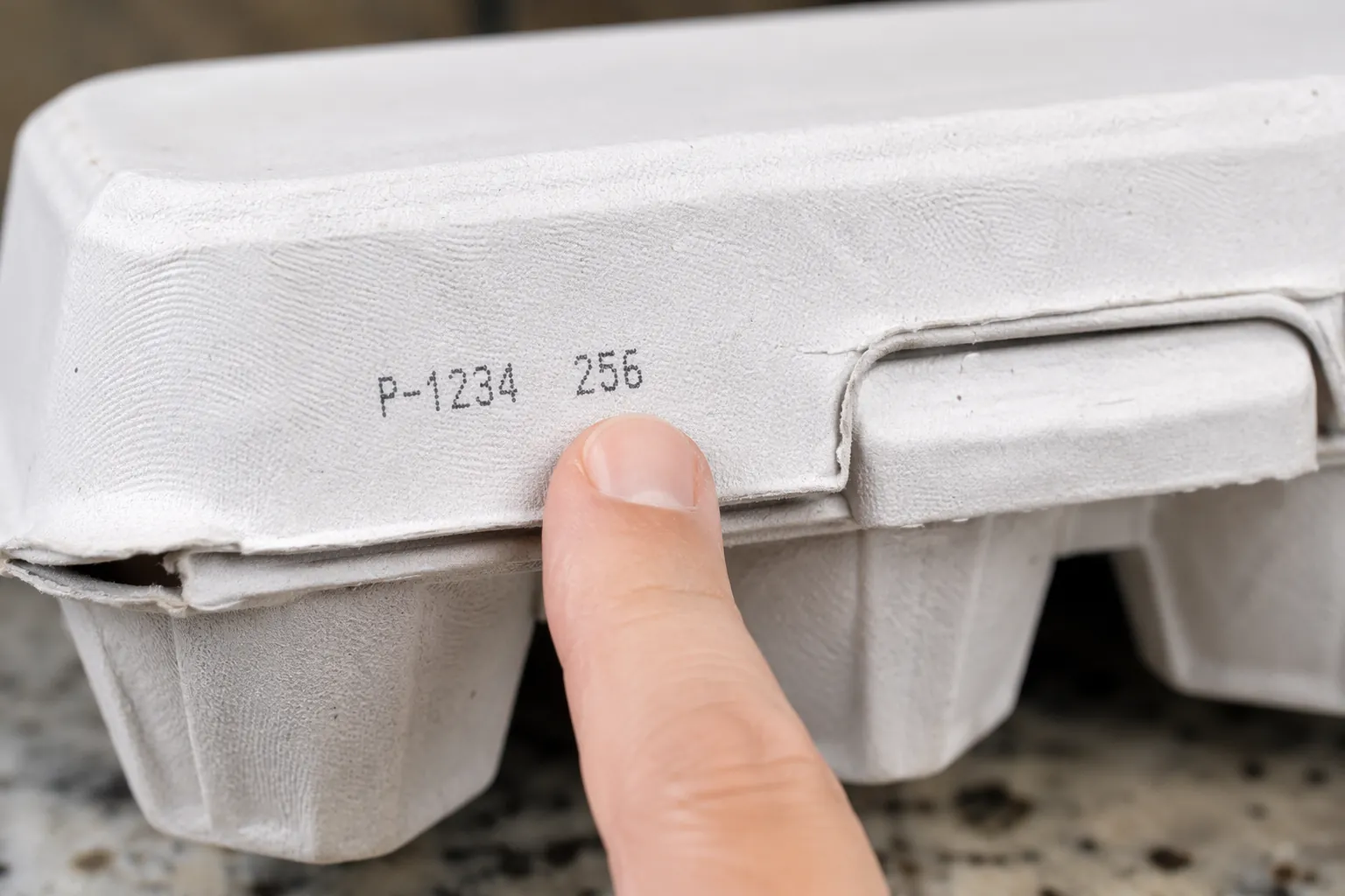 Close-up of a hand pointing to the stamped code area on an egg carton