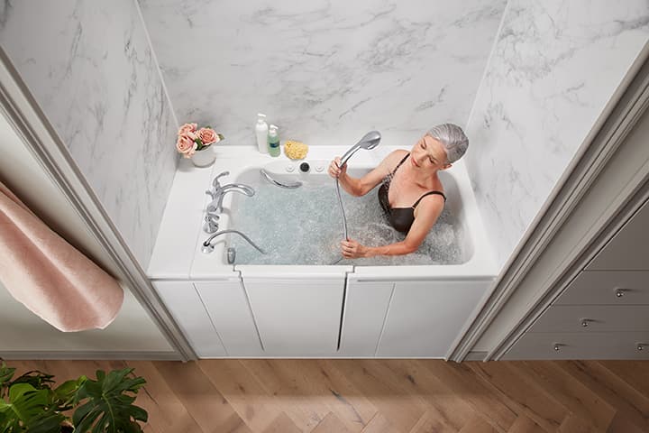 Walk-in bathtub with a closed outward-swinging door, wall grab bar, handheld shower wand, and visible low step-in threshold