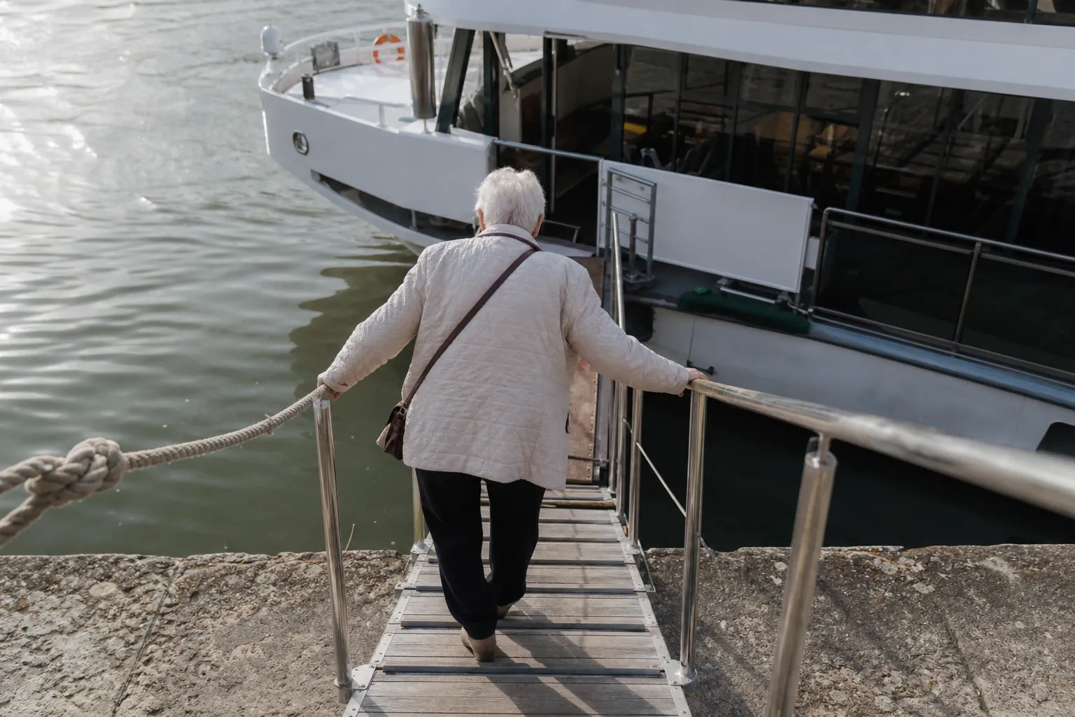Elderly passenger using both hands on a steep gangway handrail while approaching a river cruise ship