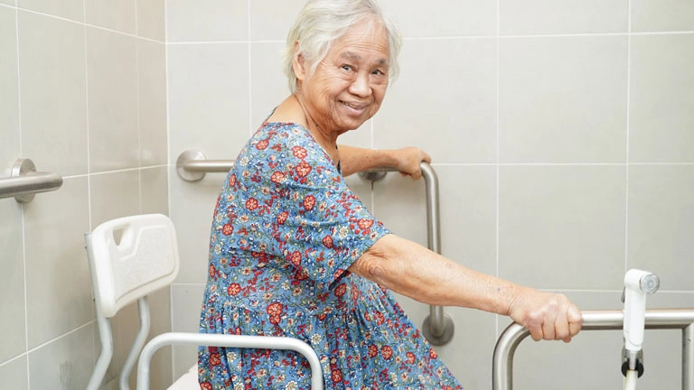 Bathroom with grab bars, shower chair, tiled shower, and non-slip bath mat