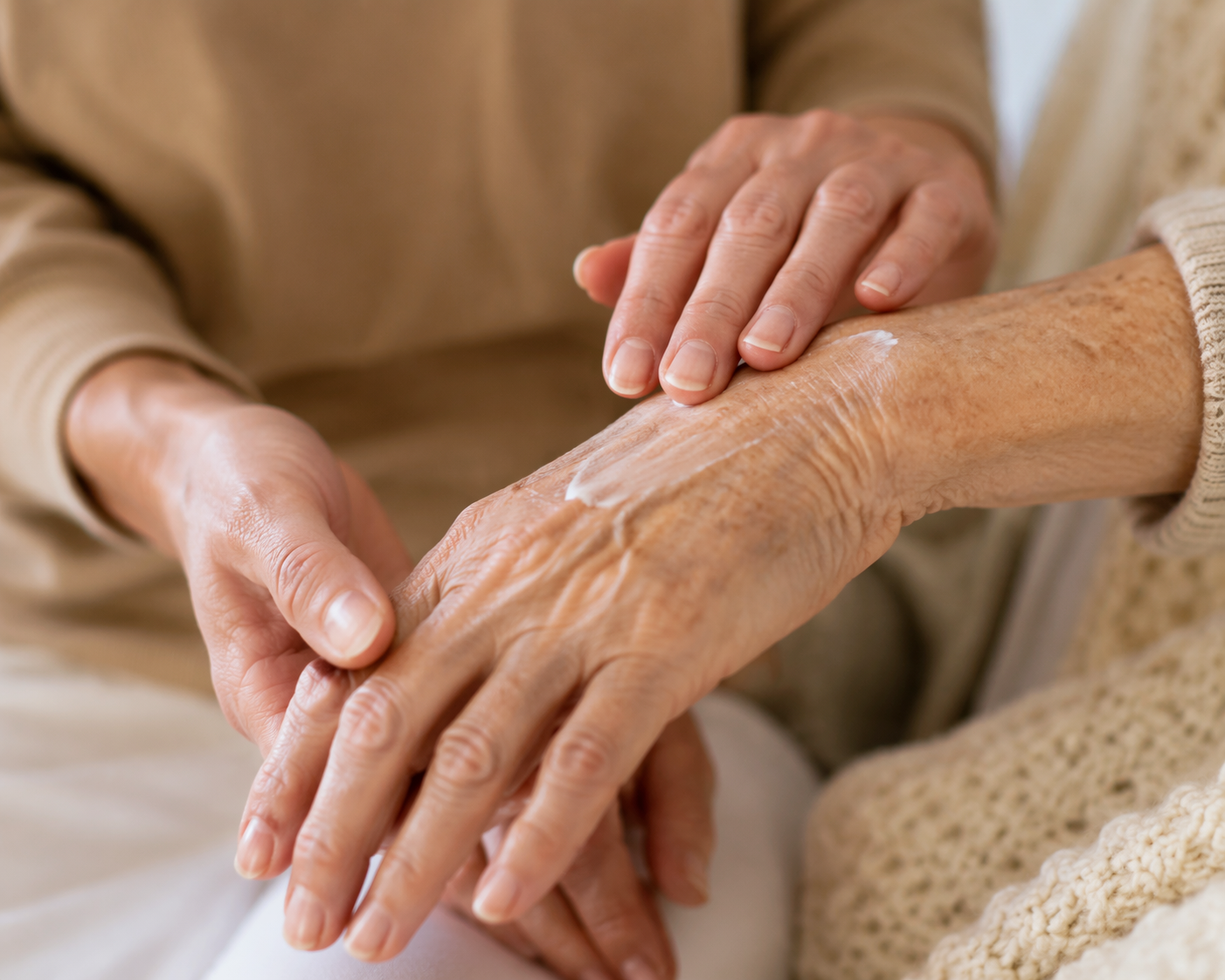 Hands gently applying cream to an older adult's thin aging skin