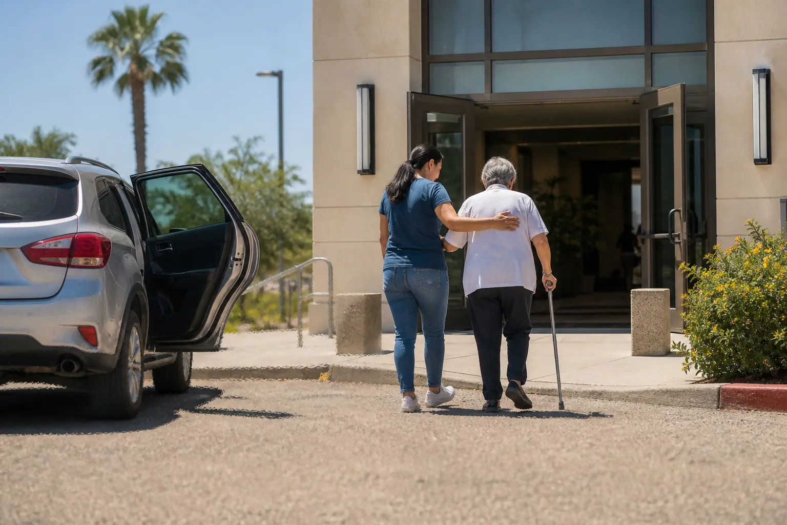 Younger adult helping an older adult walk from a hot street toward a shaded community building entrance