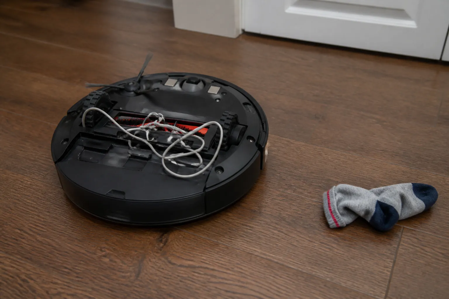 Robot vacuum tangled in a phone charging cord with a sock nearby