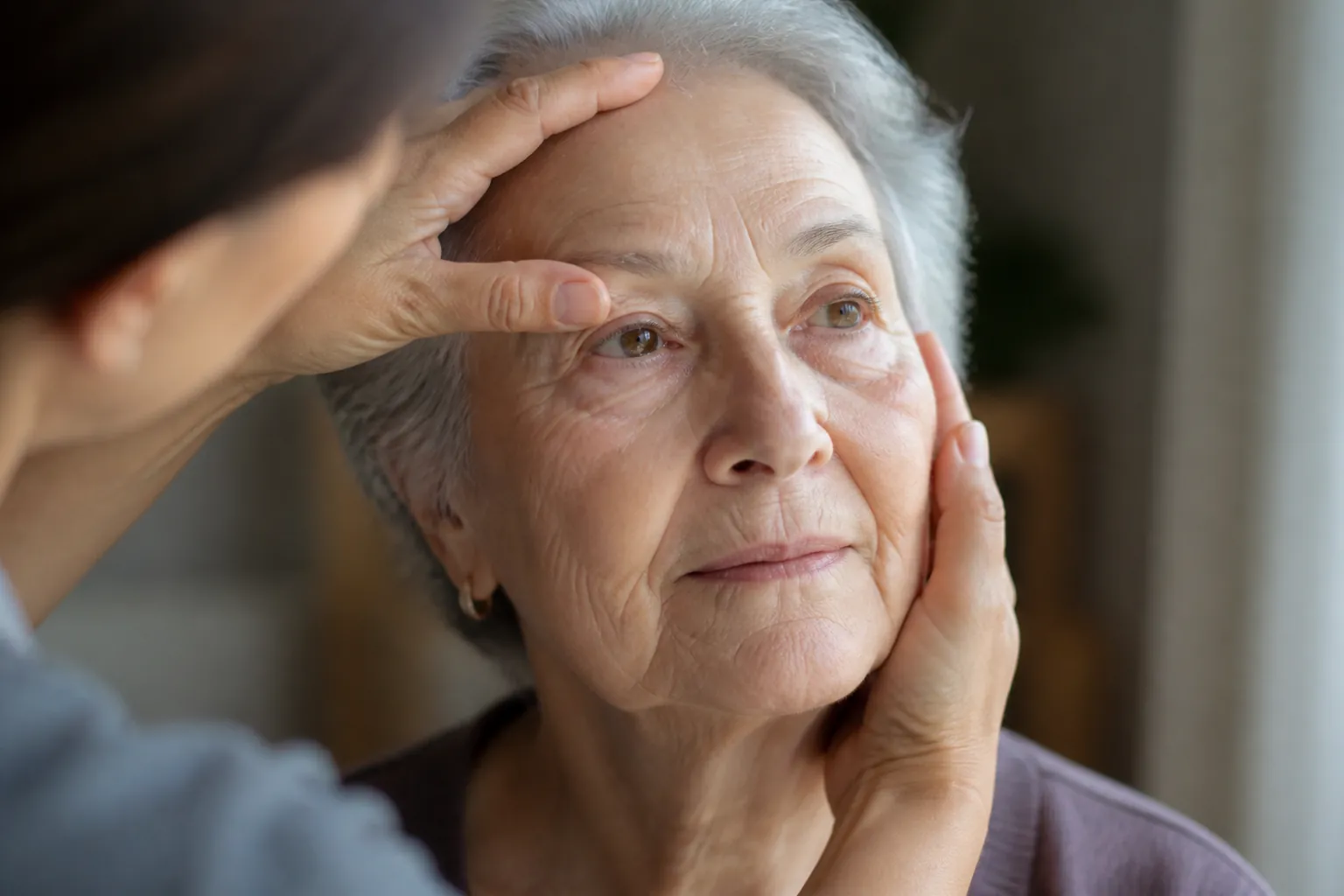 Caregiver turning an older adult's face toward window light to compare both eyes