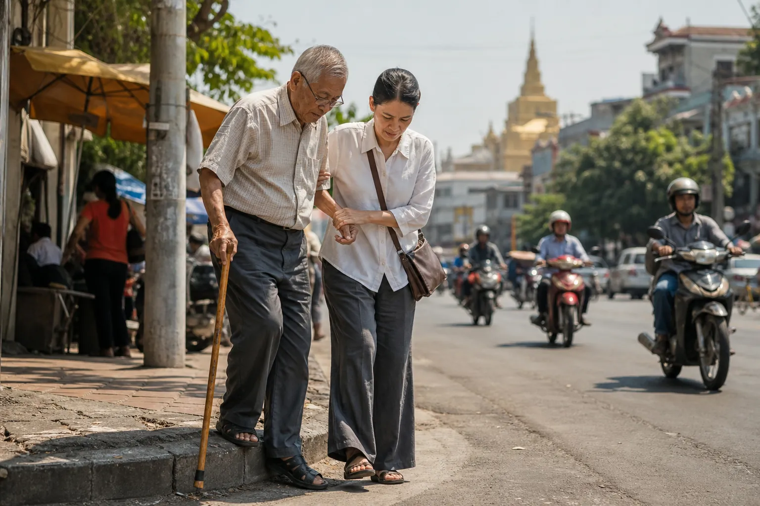 A senior man with a cane and his adult daughter stepping carefully from a curb onto an uneven Southeast Asian sidewalk as motorbikes pass