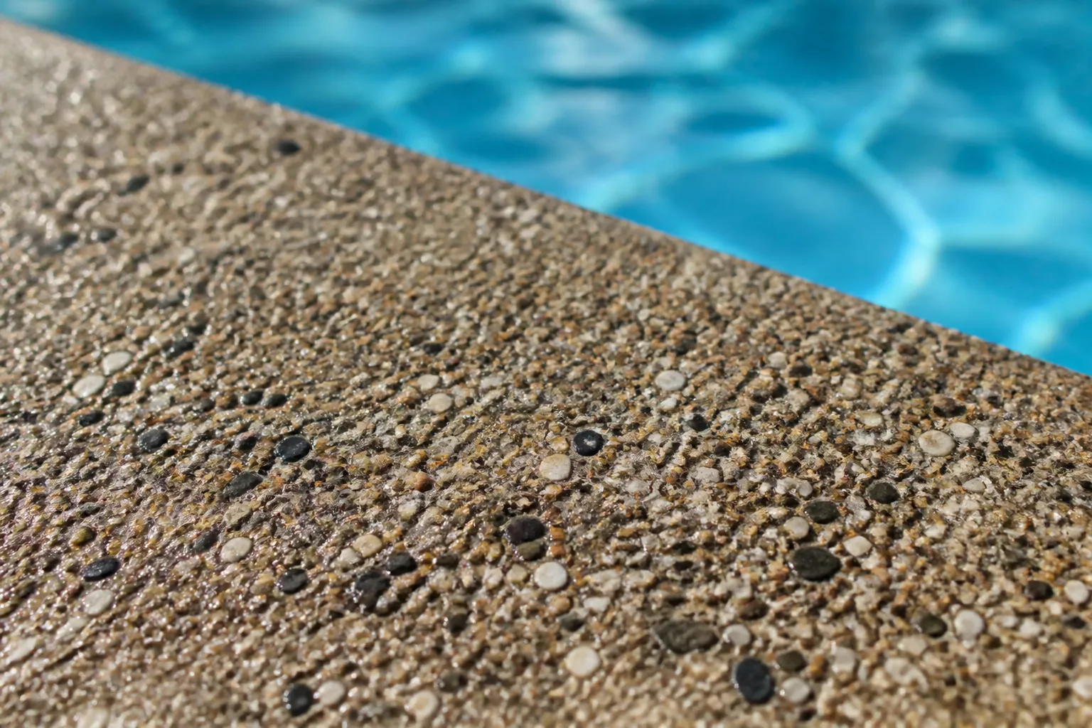 Close-up of a textured slip-resistant pool deck with water droplets near the pool edge