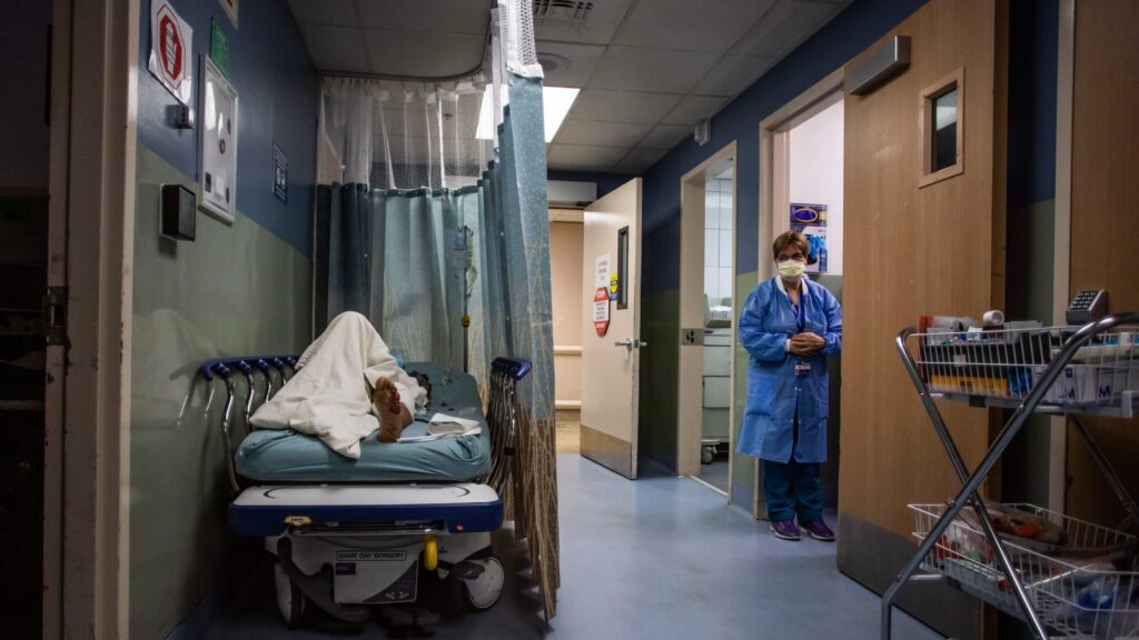 Hospital emergency room hallway with a patient waiting on a gurney under fluorescent lighting