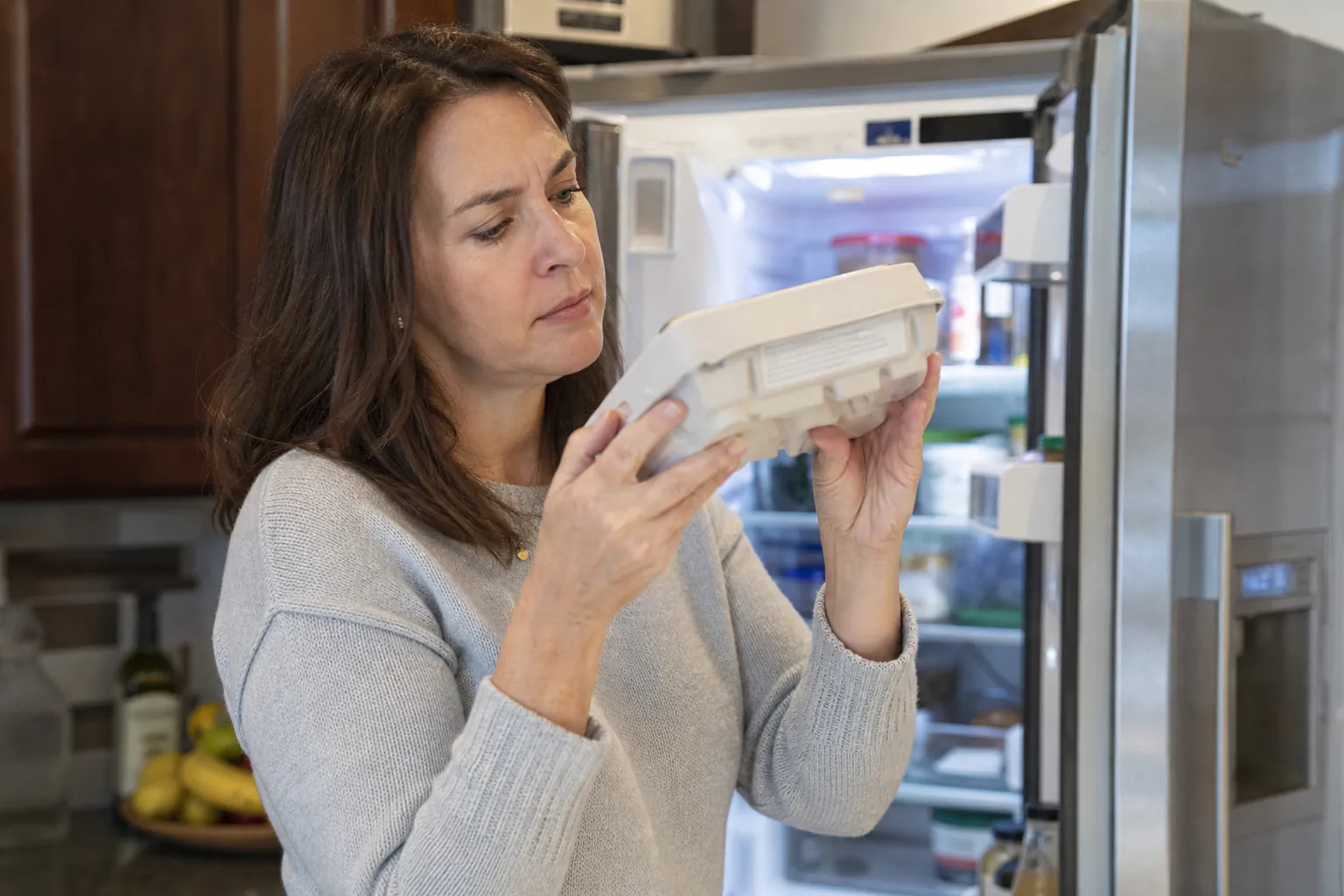 Adult daughter reading small printed codes on an egg carton at an open refrigerator