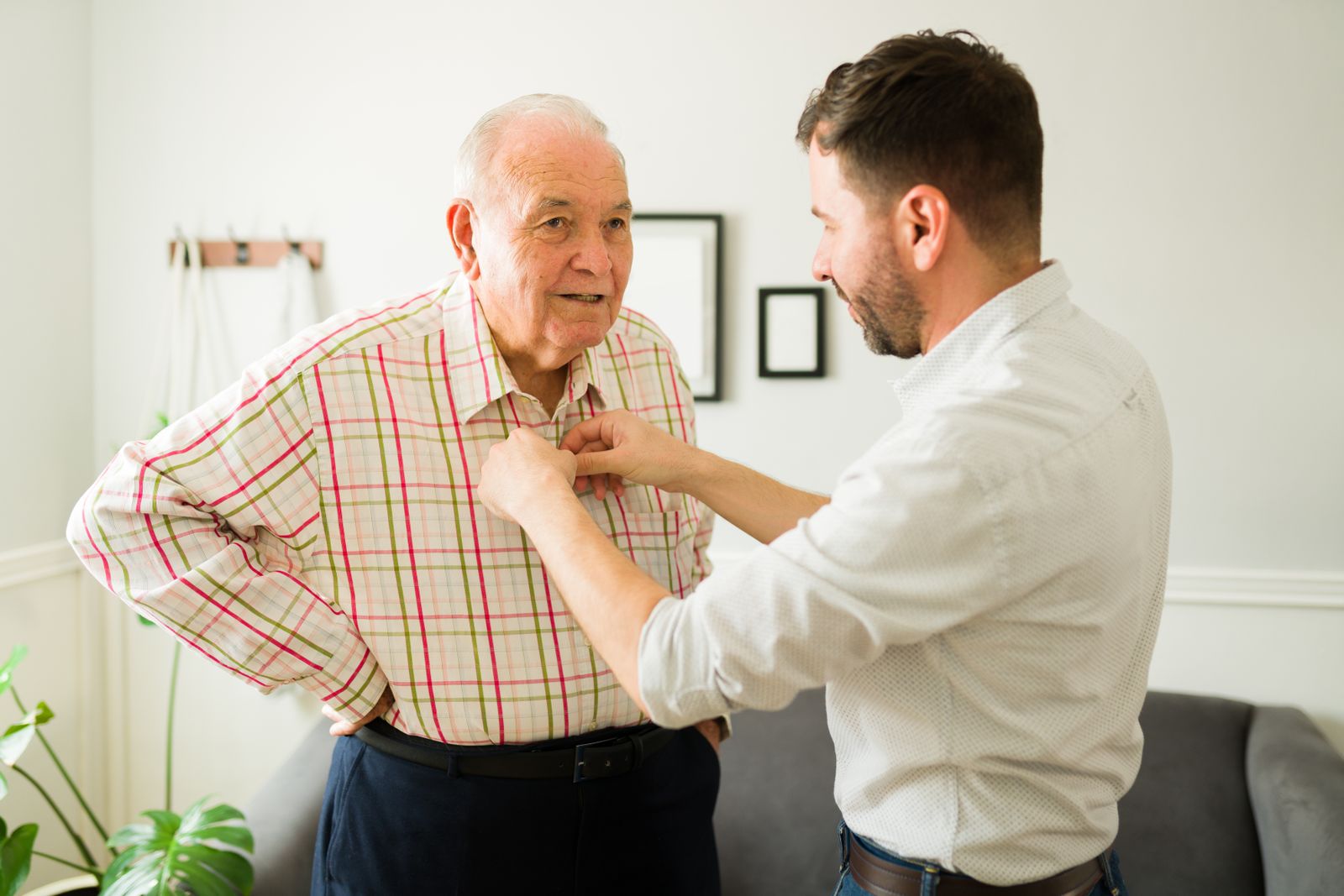 Adult child helping an older stroke survivor button a shirt at home