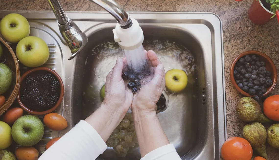 Hands rinsing fresh fruit under running water in a kitchen sink