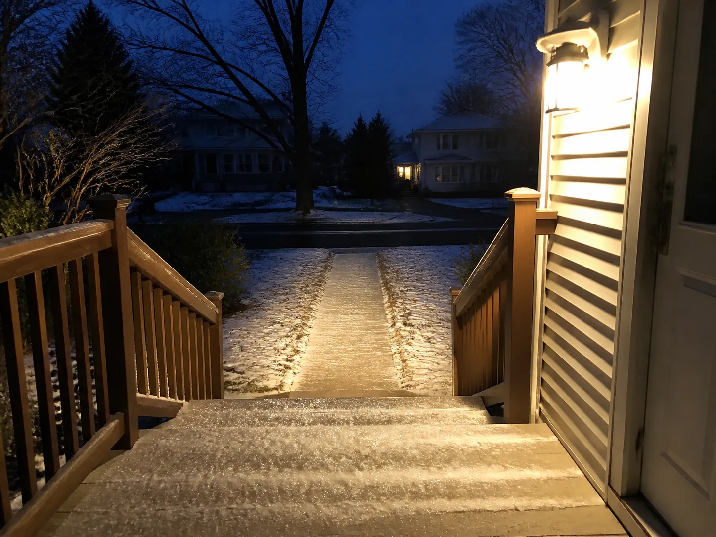 Bright porch light illuminating icy steps and a snow-dusted walkway at winter dusk