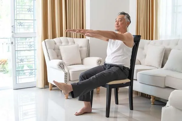 Older adult performing a seated strength exercise on a sturdy chair at home