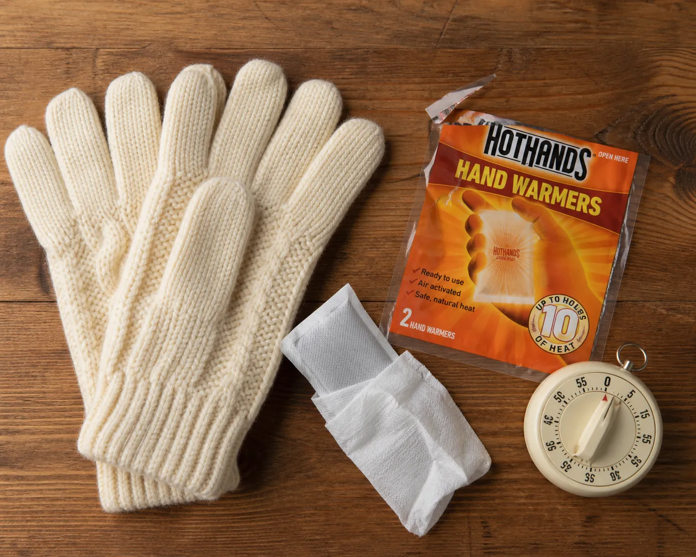 Gloves, a disposable hand warmer wrapped in cloth, and a kitchen timer on a wooden table